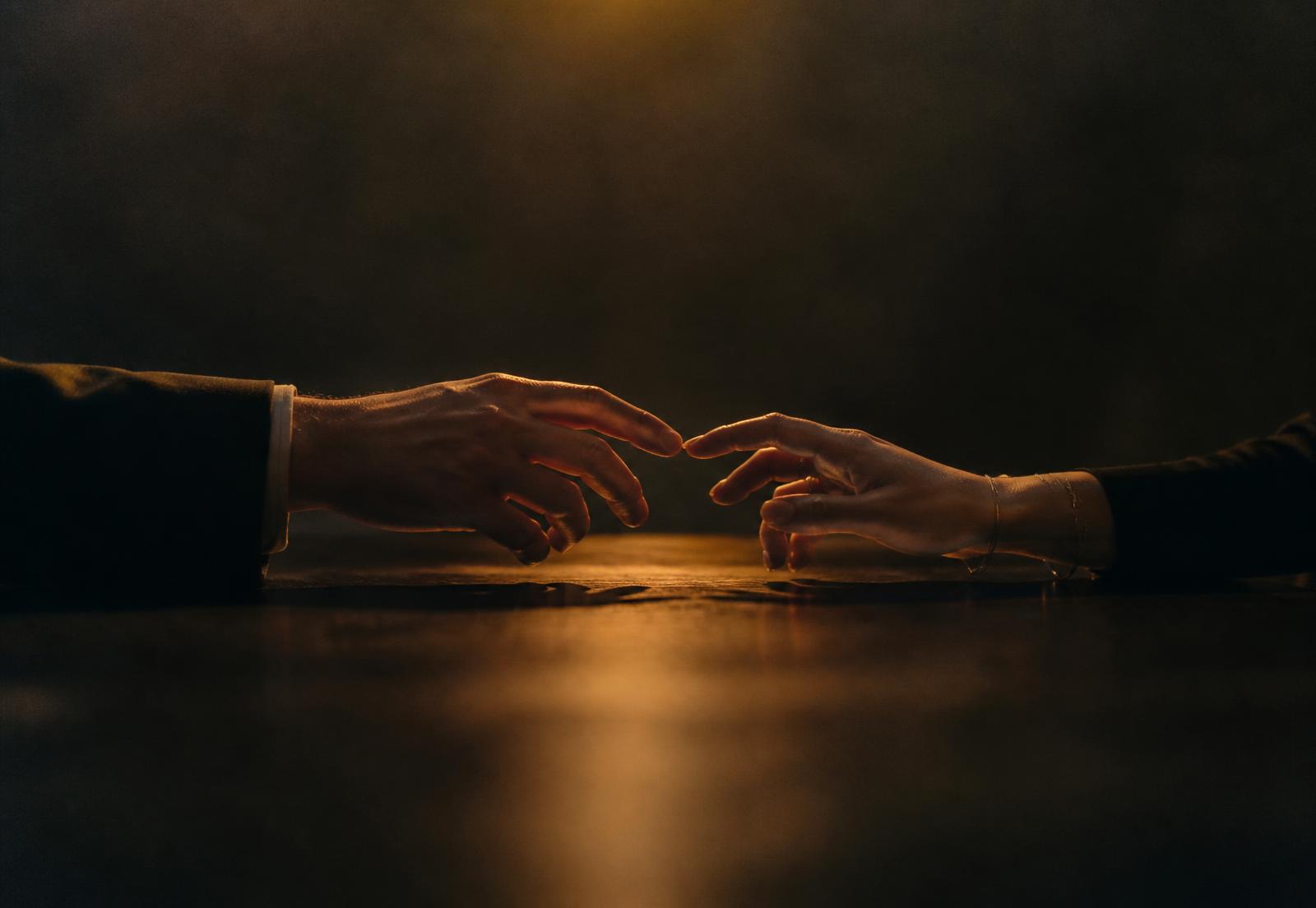 Two adults' hands reaching toward each other across a dimly lit table